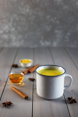 Golden milk in a mug and ingredients for its preparation on a gray wooden background. Masala Haldi Doodh.