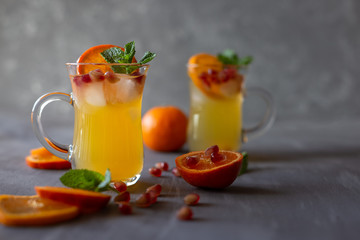 Chilled alcoholic drink with orange, mint, pomegranate and ice cubes on a gray wooden background.