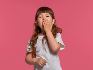 Close-up portrait of a little brunette girl dressed in a white t-shirt posing against a pink studio background. Sincere emotions concept.