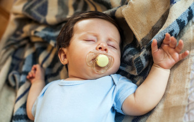 Little baby sleeping in bed at home with pacifier in mouth