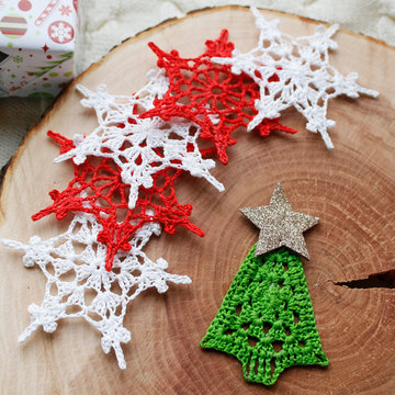 Snowflakes crocheted in different colors on a wooden log on a white knitted background. Top view. The concept of winter holidays, Christmas, New year.
