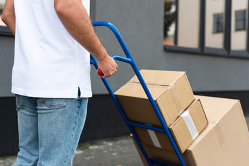 cropped view of delivery man standing with delivery cart near building