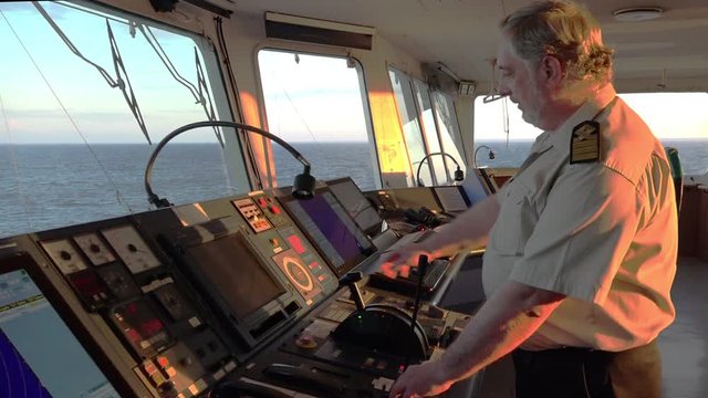 Senior ship master talks on telephone and looks at blue endless sea in vessel command post in summer evening