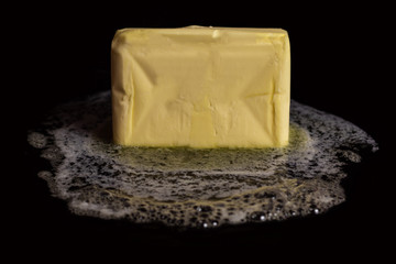 A cube of butter melting on a black plate on black isolated background.