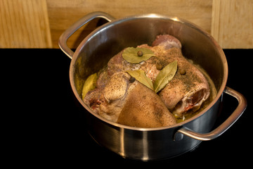 Pig knuckle in a steel pot with bay leaf, pepper and allspice on wooden background.