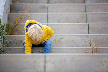 Blonde little toddler child in yellow jacket, playing on the playground