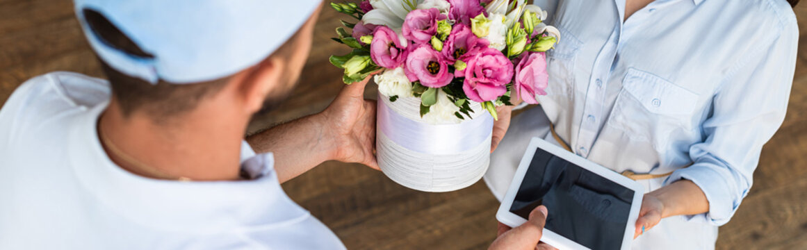 panoramic shot of delivery man giving flowers and digital tablet with blank screen to  woman