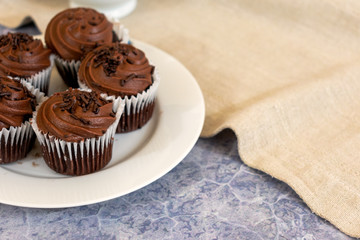 Chocolate cupcakes over white plate and tabletop on neutral blurred background with copy space