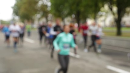 Closeup view of many blurry silhouettes of people of different ages running outdoor in park by city streets during charity marathon.