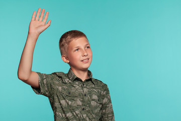 Close-up portrait of a blonde teenage boy in a green shirt with palm print posing against a blue studio background. Concept of sincere emotions. © nazarovsergey