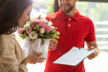 selective focus of woman smelling flowers near delivery man holding clipboard