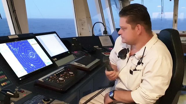 handsome first officer in white uniform talks on telephone sitting at large navigation computers and adjusts system