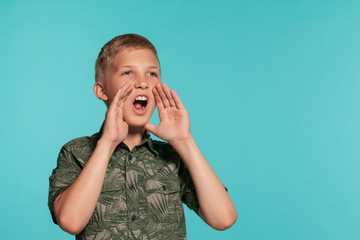 Close-up portrait of a blonde teenage boy in a green shirt with palm print posing against a blue studio background. Concept of sincere emotions.