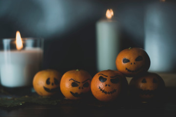 Happy Halloween citrus, tangerines painted with scary, funny faces. Dark photo with candles. Alternatives to traditional Halloween pumpkins.