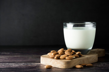 Almond milk - alternative to clasic milk. A glass with almond milk and almond nuts. Dark food photo with copy space. Healthy, vegan milk.