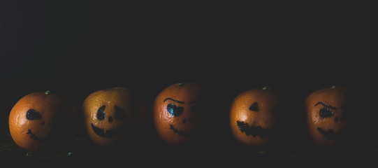 Happy Halloween citrus, tangerines painted with scary, funny faces. Dark photo with copy space.