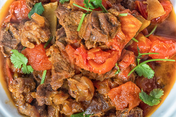Veal stewed with vegetables in tomato sauce on a black concrete or stone background.