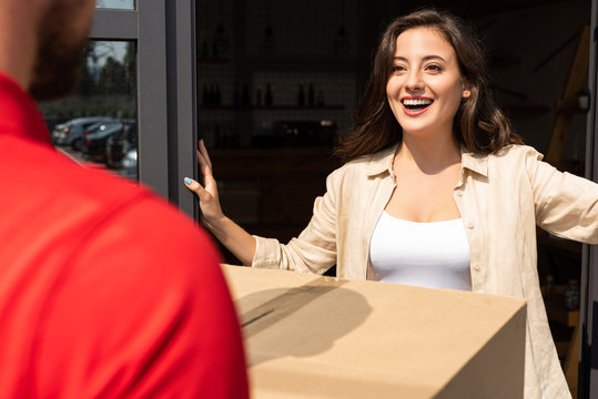 selective focus of positive girl looking at delivery man with box