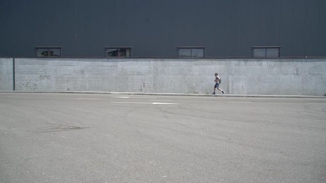 Fair-skinned young guy walks along a gray fence in an industrial area