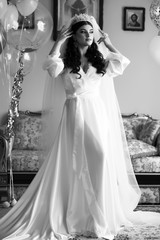 Beautiful bride in white wedding robe on the background of sofa with air balls in the room.  Beautiful veil flutters. ful happy bride preparing for her wedding. Black and white