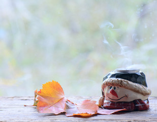 decorative candlestick - a snowman stands near the autumn leaves. Smoke from the extinguished candle rises above it.