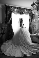 Gorgeous brunette woman with long wedding dress in luxury interior of living room. Beauty, fashion. Bride with elegant hairstyle and makeup. Beautiful happy bride preparing. Black and white