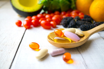Pills and capsules in wooden spoon with fresh fruits.Vitamins and supplement from fruits concept.
