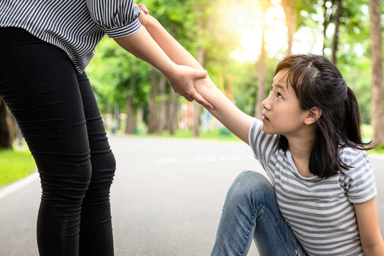 Passerby Helping To Support The Child Girl To Stand Up From On The Floor After Falling Down At Park,asian Woman Pulling Hand And Give Encouragement To Female Teenage,kindness,friendship Concept