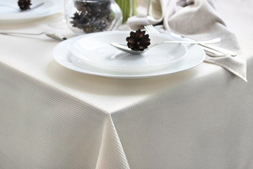 photo of a festively served table, the corner of the table with a plate is cropped. light dishes and a tablecloth. Decor Christmas cones.