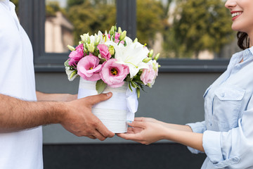 cropped view smiling girl receiving flowers from delivery man outside