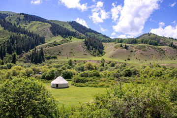 White yurt on jailoo against the background of mountains covered by forest and sky with clouds....