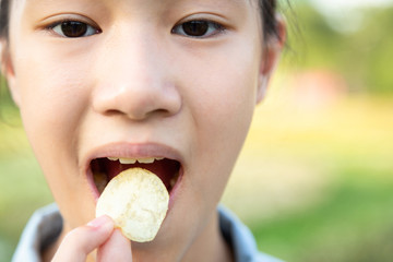 Closeup,bad food,asian child girl eating potato chips, female teenager puts crisps potato chip in...