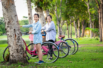Happiness asian mother and daughter standing near their bicycle in green nature at outdoor park,beautiful smiling child girl and happy woman is resting on holiday,health care,ecology lifestyle concept