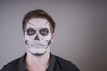 Portrait of a young serious guy with a painted skeleton mask on his face. Preparing for Halloween. Copy space