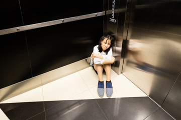 Asian child girl is stuck in an elevator,sad teenager girl sitting alone is crying in a despair with claustrophobia in elevator,worried woman is experiencing fear,stress,anxious and waiting for help