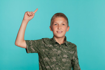 Close-up portrait of a blonde teenage boy in a green shirt with palm print posing against a blue studio background. Concept of sincere emotions.