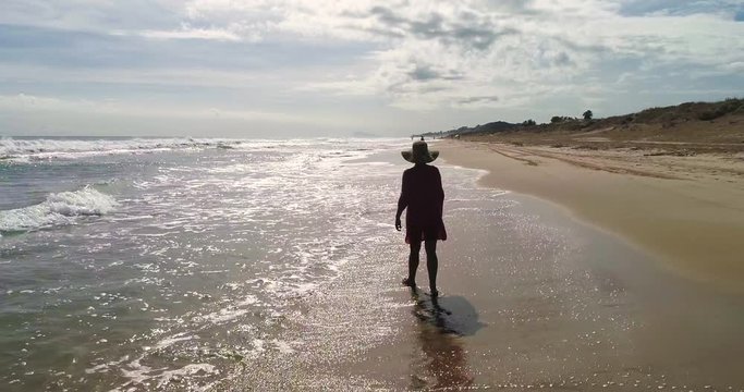 Silueta de mujer en la orilla de una playa de arena gravado por dron
