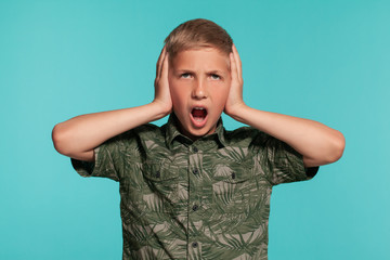 Close-up portrait of a blonde teenage boy in a green shirt with palm print posing against a blue studio background. Concept of sincere emotions.