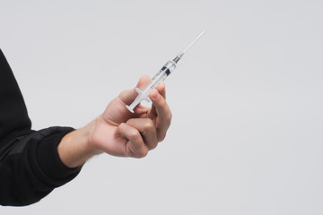 Man's hand hold a syringe with liquid. Guy in a black hoodie on a white background. Person offers you drug or medical treatment. Drug addict. Dangerous self-medication. Copy space.