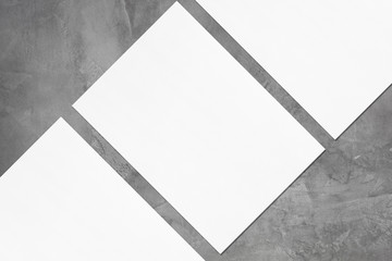 Closeup of three empty white rectangle poster mockups lying diagonally with soft shadow on dark grey concrete background. Flat lay, top view. Open composition.