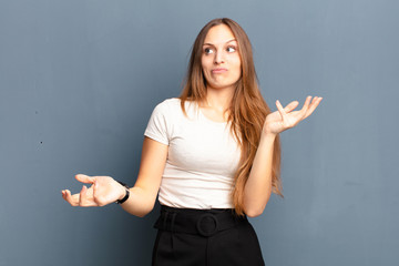 young pretty woman shrugging with a dumb, crazy, confused, puzzled expression, feeling annoyed and...