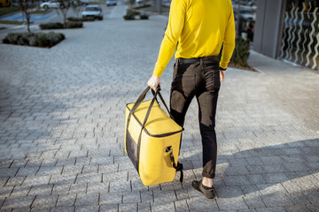 Courier carrying yellow thermal bag, delivering food in the city, close-up view with copy space. Delivery service concept