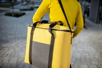 Courier carrying yellow thermal bag, delivering food in the city, close-up view with copy space....