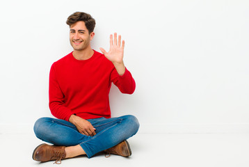 young handsome man smiling happily and cheerfully, waving hand, welcoming and greeting you, or...