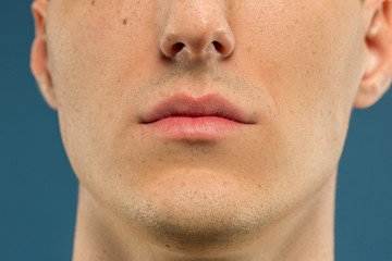 Caucasian young man's close up shot on blue studio background. Beautiful model with well-kept skin. Concept of human emotions, facial expression, sales, ad, male beauty and healthcare. Lips and cheeks