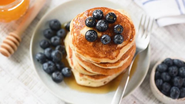 Pancakes with blueberries and maple syrup on white plate. Rotating table with tasty breakfast food