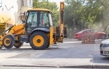 Orange excavator on wheels works in the city