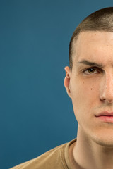 Caucasian young man's close up shot on blue studio background. Beautiful male model in shirt. Concept of human emotions, facial expression, sales, ad. Looks serious, confident.