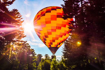 Hot air balloon flying close to the ground with trees and sky