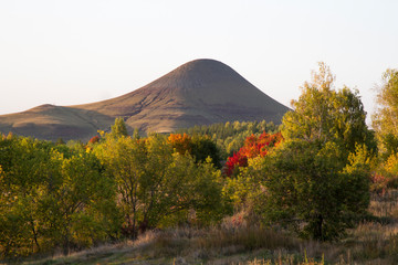 A single mountain surrounded by deciduous and coniferous trees.